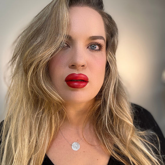 Woman with long blonde hair and red lipstick wearing a black top. lip filler. lip prosthetic