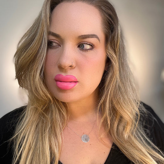 Woman with long blonde hair and pink lipstick wearing a black top against a neutral background. lip filler prosthetic